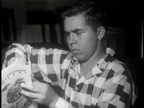Young man sitting indoors and reading a magazine titled The Log, 1951