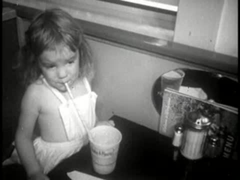young girl drinking from a cup with a straw at a table