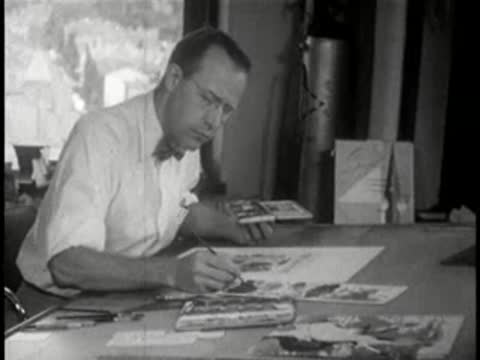 Man sitting at a large table, sketching or drawing illustrations with a brush