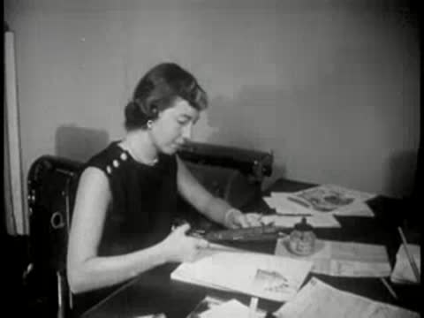 Woman sitting at office desk, using scissors to cut paper documents