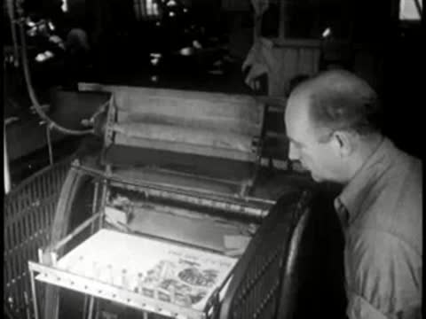 Worker checking finished printed materials coming off a press, mid-century.