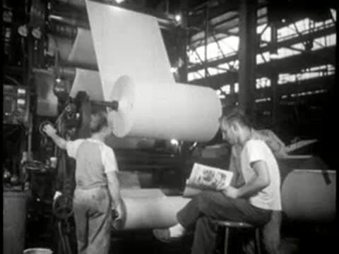 Workers sitting by massive paper rolls in a paper mill, mid-century.