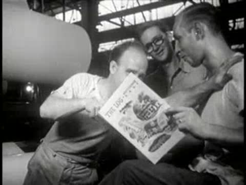 Workers inspecting a newly printed magazine together in a factory, mid-century.