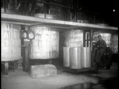 Factory interior showing large storage containers and materials, mid-century.