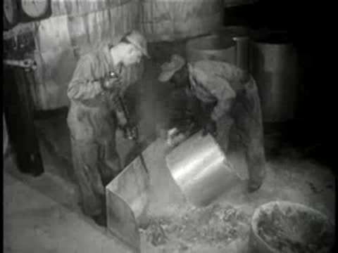 Workers processing materials using heavy machinery in a factory, mid-century.