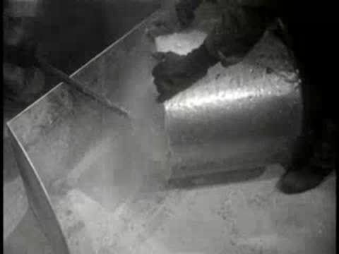 Close-up of workers using industrial equipment in a factory setting, mid-century.