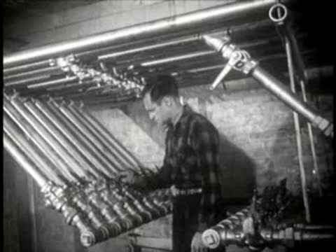 Worker operating a complex system of industrial pipes and valves, mid-century.