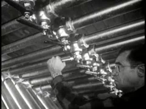 Close-up of a worker adjusting valves on industrial pipes, mid-century.