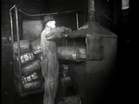 Worker loading heavy sacks into an industrial furnace or incinerator, mid-century.
