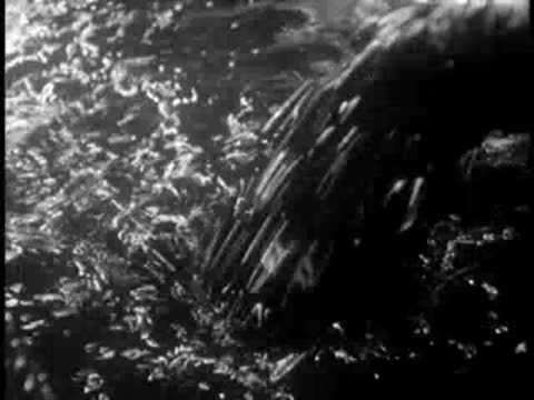 Dark liquid pours heavily from a pipe into a large vat of mixture.