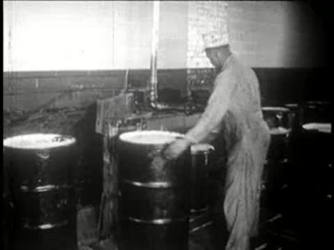 Worker positions a large metal barrel near machinery in a plant.