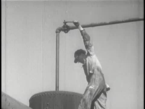 Worker turns a high overhead valve connected to a large industrial tank.