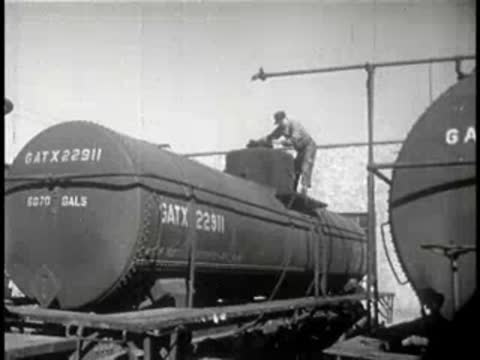 Wide view of workers operating around large industrial tank cars on rails.