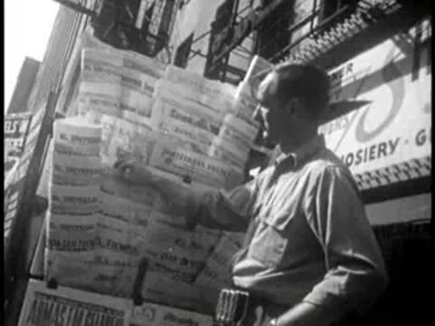 Man examines a display rack filled with various newspapers.
