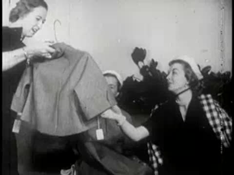 Woman presents a folded garment to another woman seated indoors.