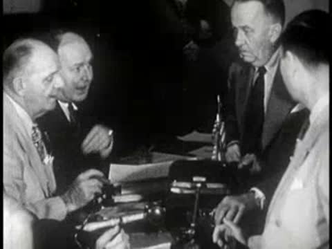 Three men in suits seated around a conference table with documents.