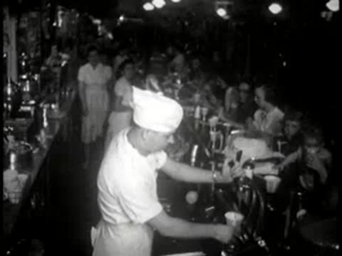A soda jerk working behind a diner counter dispensing drinks.
