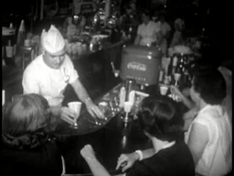 A soda jerk serving customers at a crowded diner counter.