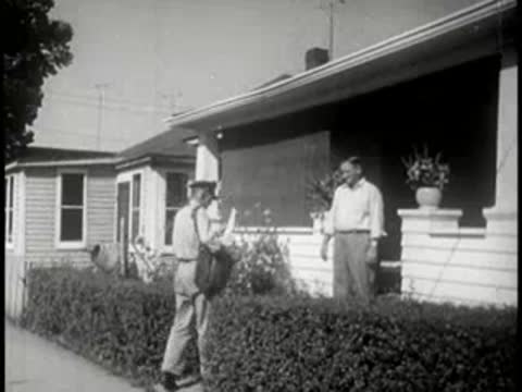 Postman walking up residential path and delivering mail to a man at a house