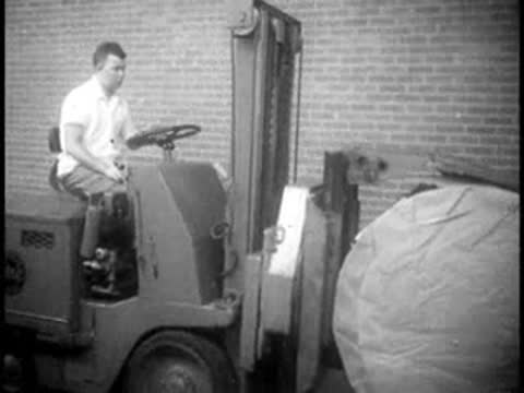 A factory worker operating a forklift carrying a large paper roll.