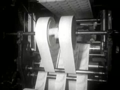 Paper machine rollers feeding white paper web in a manufacturing plant.