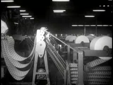 Industrial rollers processing paper webs across a factory floor.