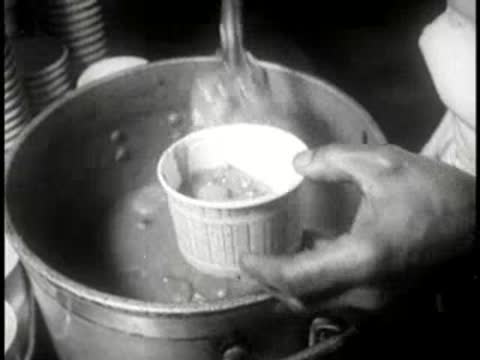 Close-up of a chef scooping food into single-use paper cups.