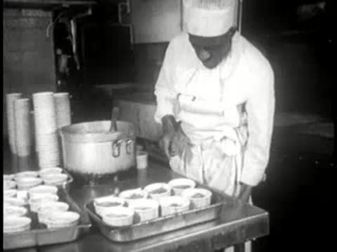 A chef plating food into multiple single-use cups in a restaurant kitchen.