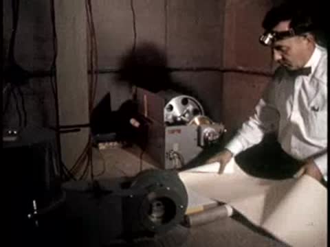 A technician unrolls paper in front of a recording device, retro 1950s office