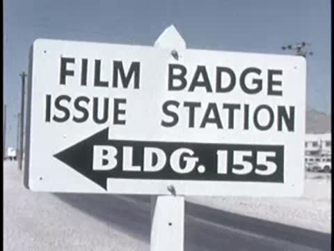 A white sign reading 'Film Badge Issue Station Bldg. 155' pointing left with an arrow