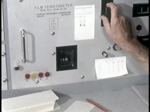 A person holding a perforated film badge card next to a control panel, then panning to clouds