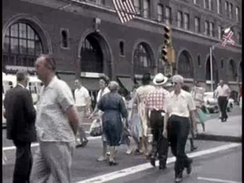 Crowd of people walking on busy city street in mid-century.