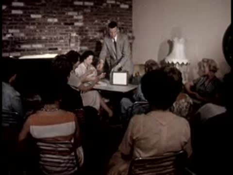 A man presents a device at the front of a room with seated women