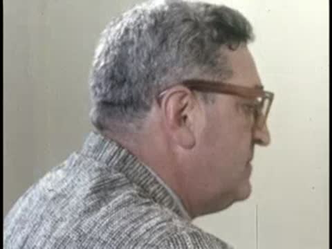 Profile view of a man wearing glasses, seated indoors, 1950s professional style