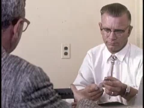 Two men exchange a small item across a desk, retro office setting