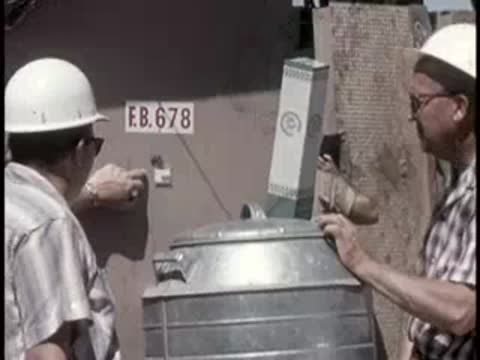 two men in hard hats inspecting equipment next to a metal container outdoors