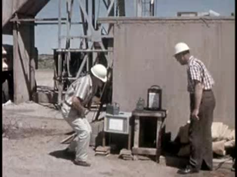 two men in hard hats setting up scientific equipment near a building