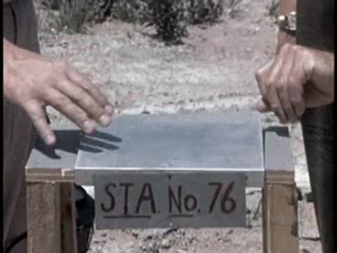 hands operating scientific measuring equipment on a wooden stand labeled STA No 76