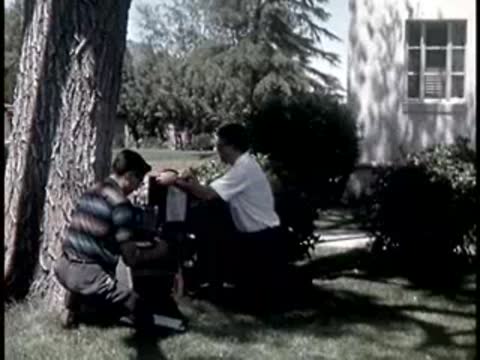 two men sitting under a large tree packing up scientific equipment