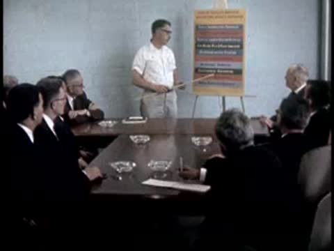A man presents a chart to seated men in a conference room