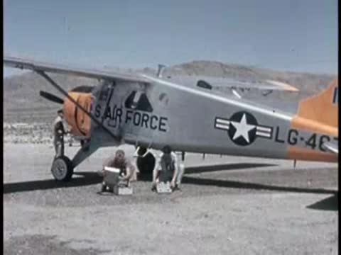 two men loading equipment near a small US Air Force airplane outdoors