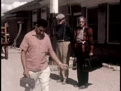 three people walking outdoors in a desert area carrying equipment cases