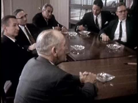 Seated men in a conference room listen to a presentation, 1950s business attire