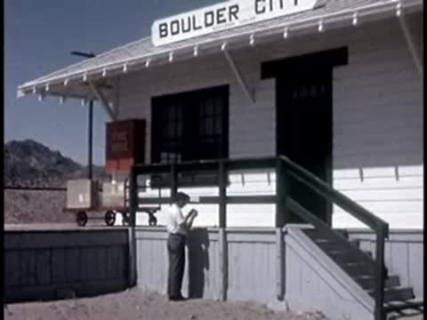 person standing on porch of "Boulder City" railway station building
