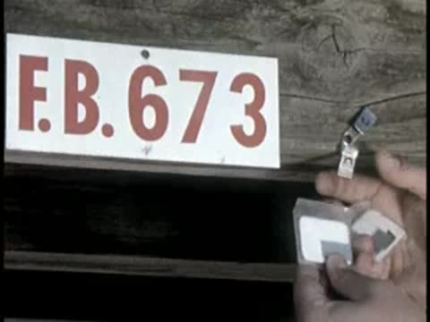 hand holding small tag in front of sign reading "E.B. 673"
