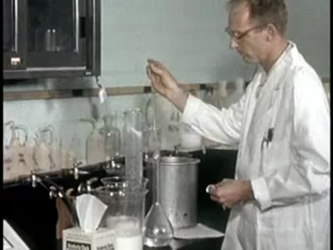 worker in white coat pipetting liquid into glassware in laboratory