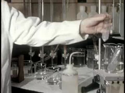 A technician in a white coat moves a small test tube in a laboratory.