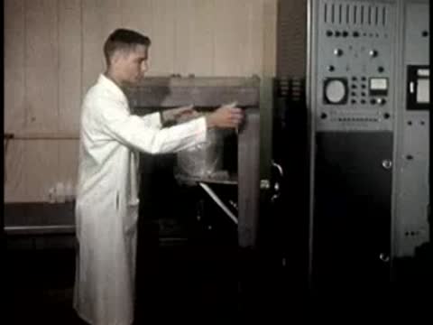 A technician in a white coat operates a large piece of industrial laboratory equipment.