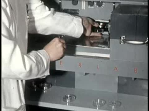 Hands operate a piece of mechanical laboratory machinery with sliding drawers.