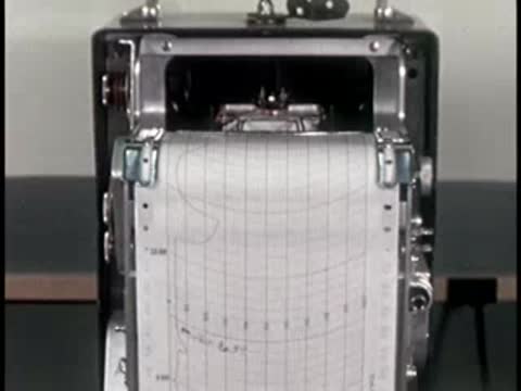 A close-up of a recording chart machine plotting graphs on moving paper.